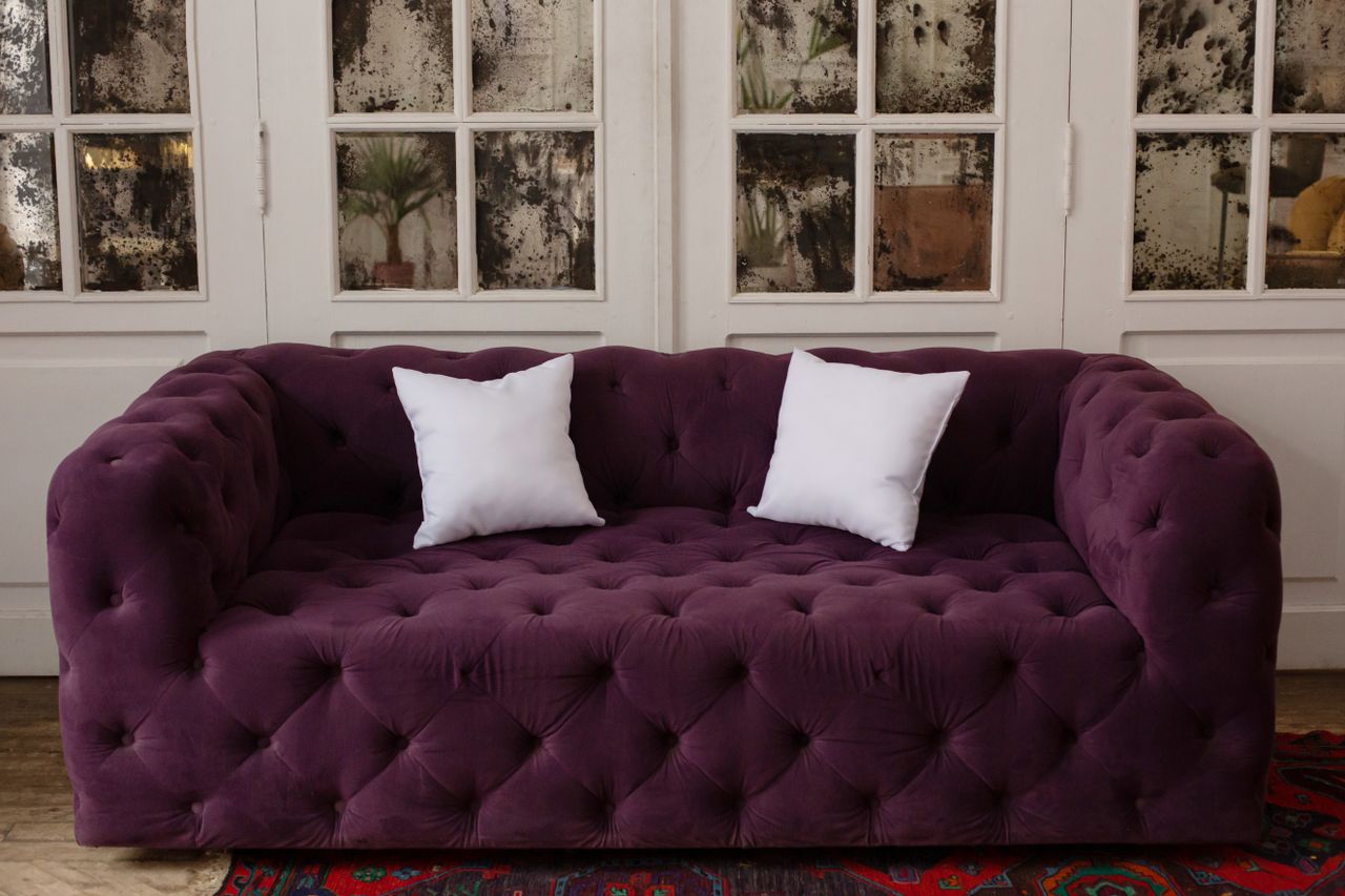 About Luxurious purple tufted sofa with white cushions in a stylish, cozy indoor setting.